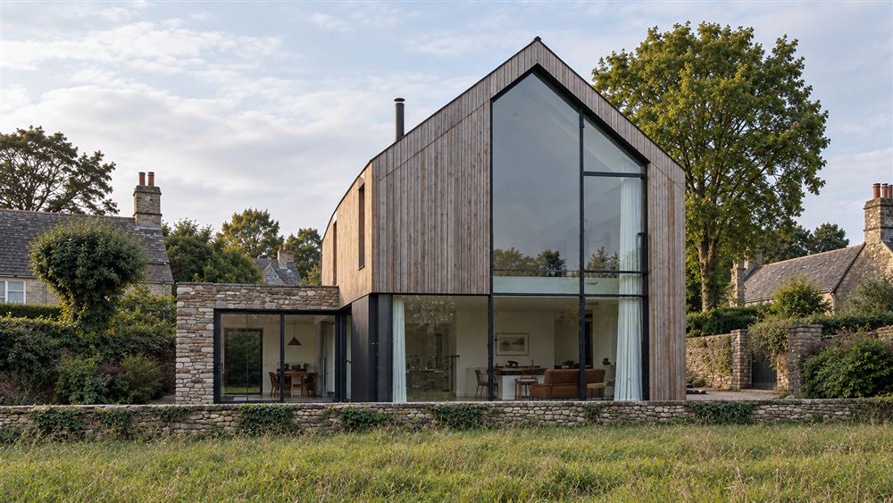 The Barn: a timber-clad gabled house with a tall glazed end beside a stone wall in an English village