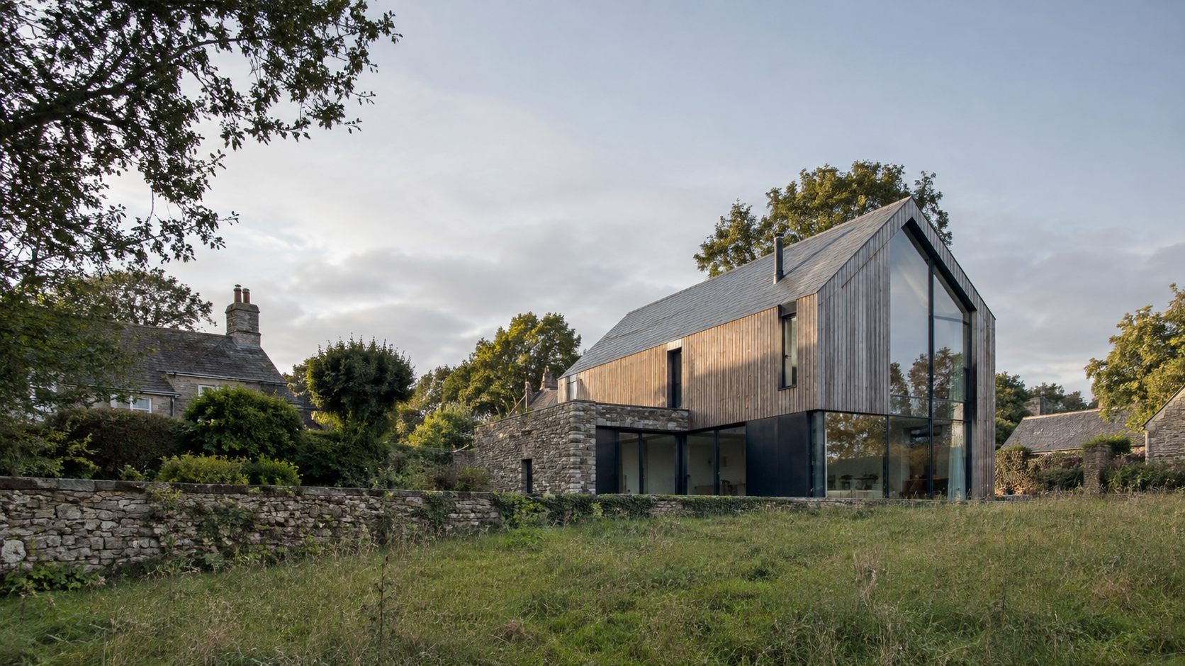 The Barn: a timber-clad gabled house with a tall glazed end beside a stone wall in an English village